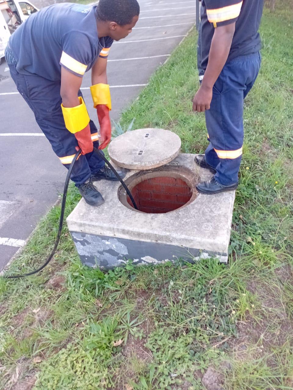 Plumbers opening a drainage manhole for inspection